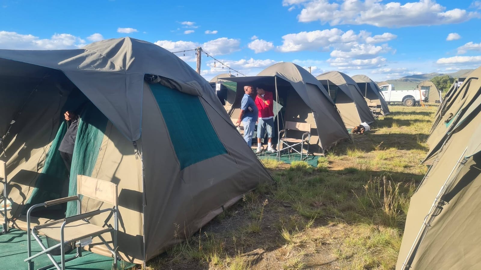 Rows of camping tents and chairs on grass beneath a blue sky
