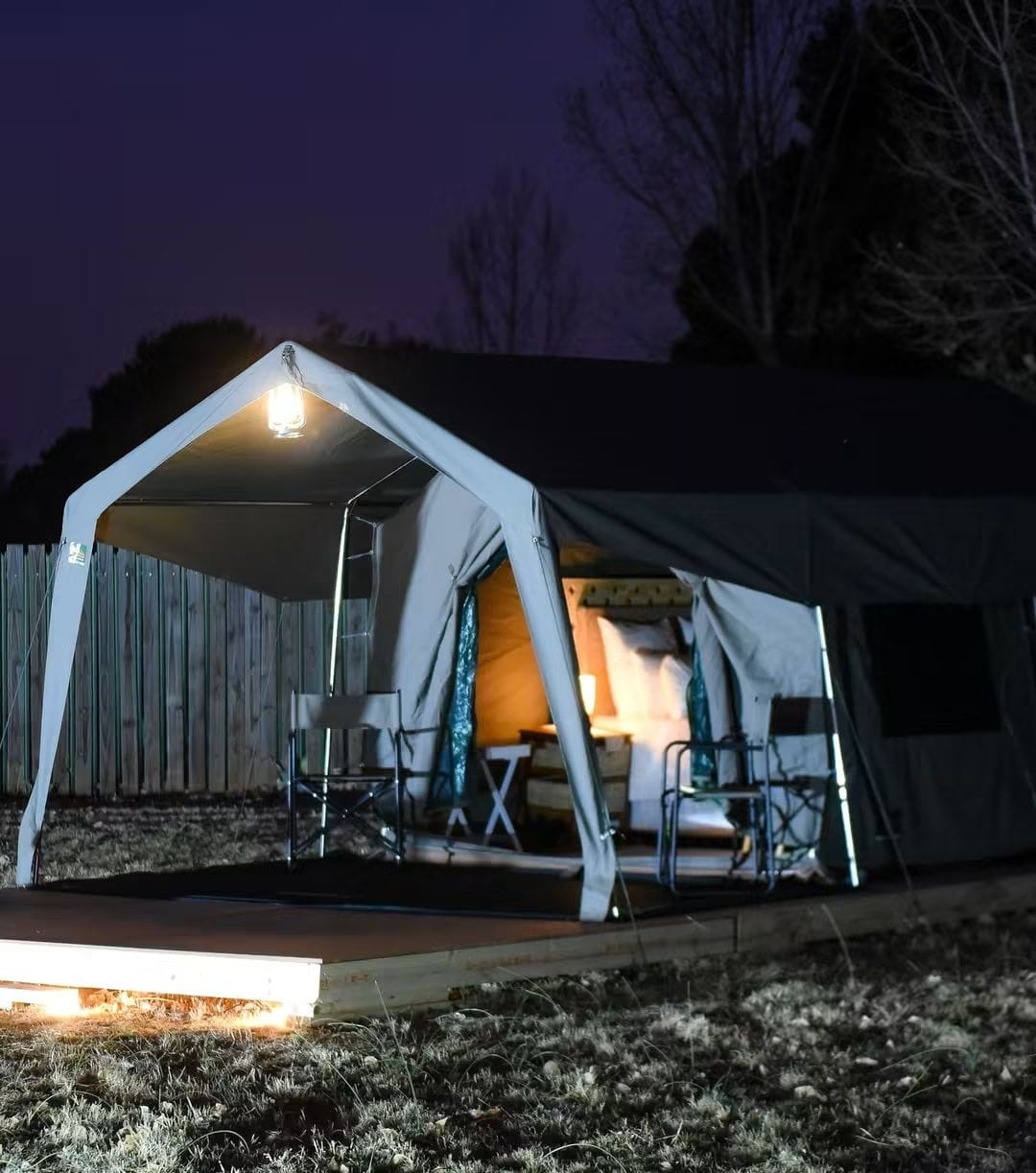An illuminated glamping tent with a covered veranda at night