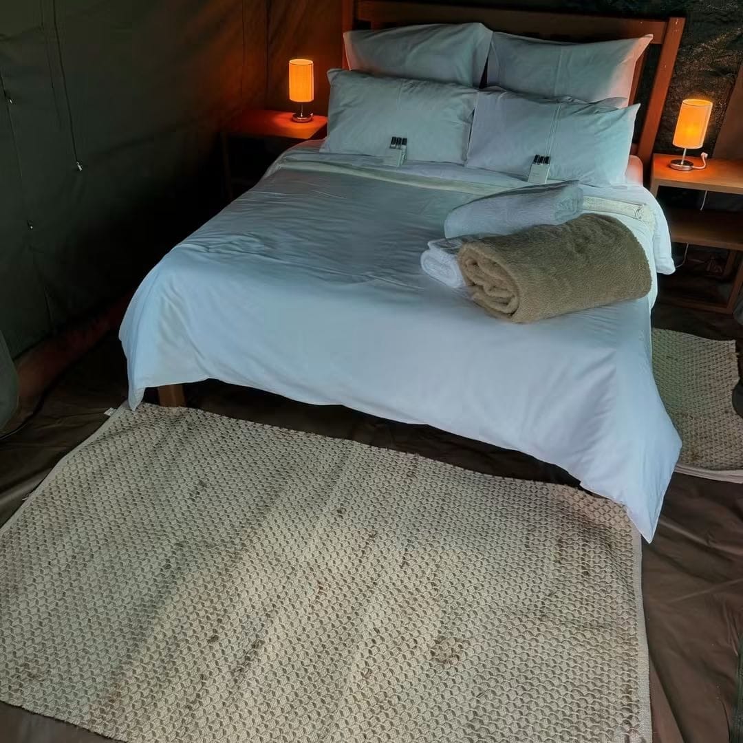 A made-up glamping bed with folded towels, bedside tables and soft lighting